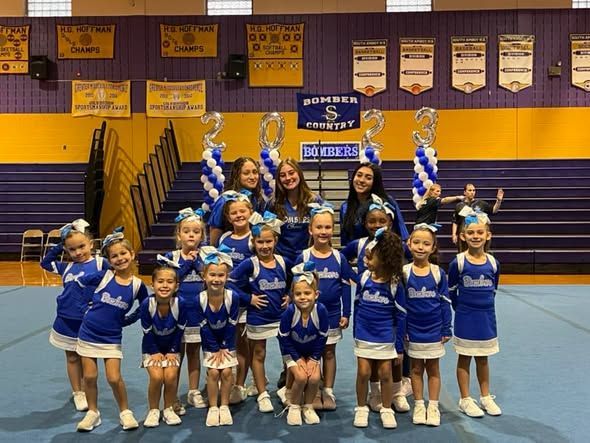 Cheerleading squad in blue and white uniforms holding trophies in a gym.