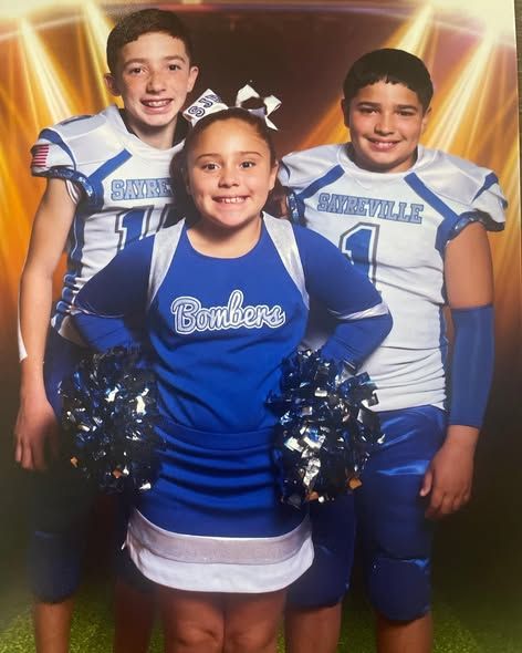 Three children: two football players flanking a cheerleader in blue uniforms, smiling.