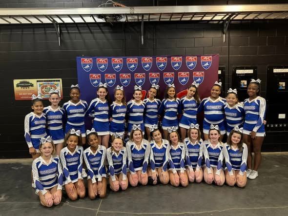 Cheerleading team in blue and white uniforms posing in front of a banner.