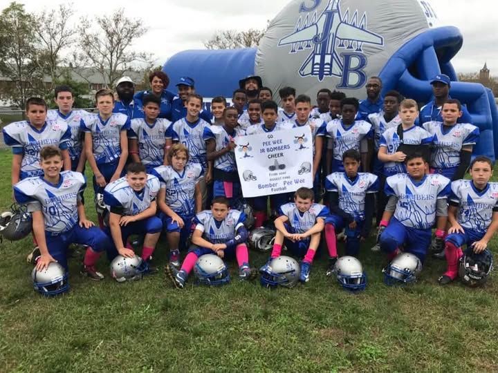Youth football team in blue and white uniforms pose with a banner on a grassy field in front of an inflatable structure.