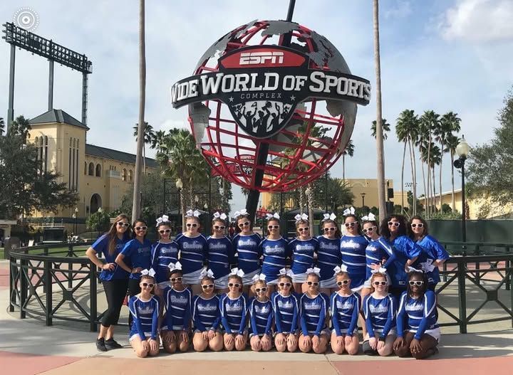 Cheerleading squad poses in front of the ESPN Wide World of Sports Complex globe. They wear blue and white uniforms.