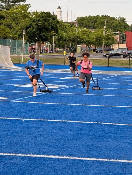 Three people pulling weighted sleds on a blue track, training outdoors.