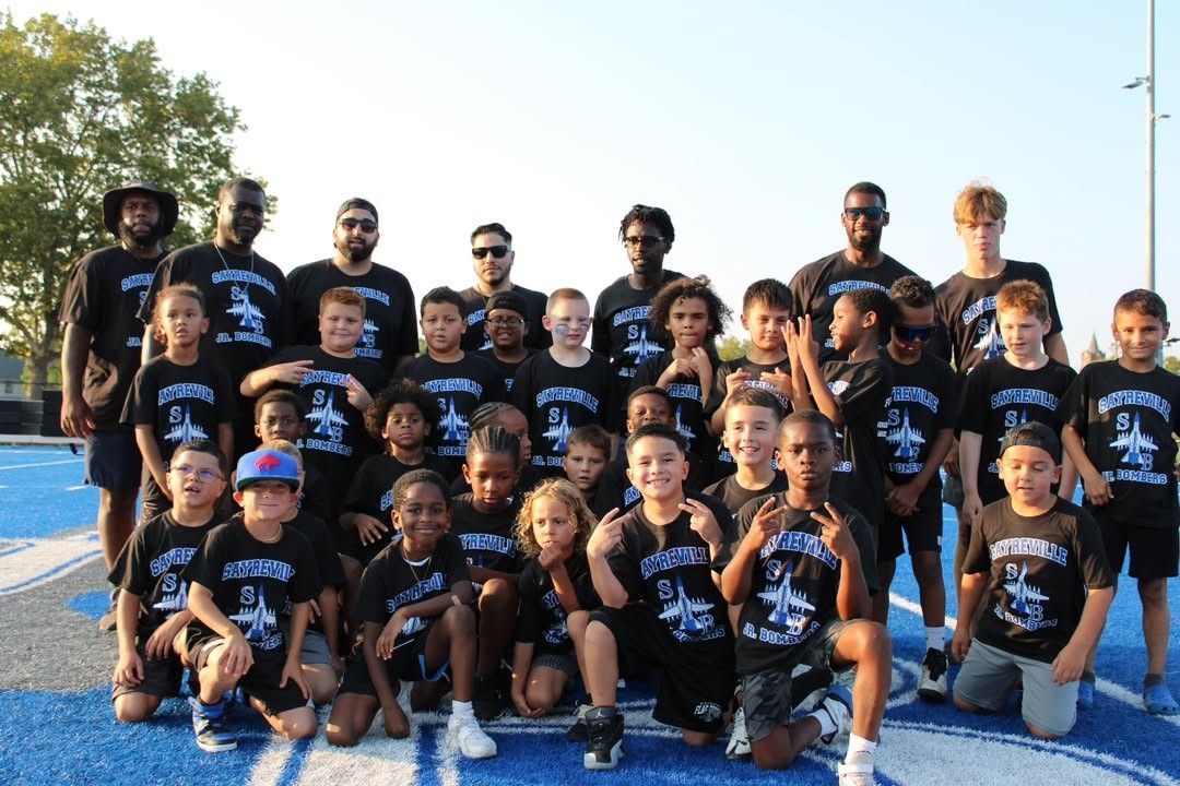 Youth football team poses on a blue track, wearing black jerseys.