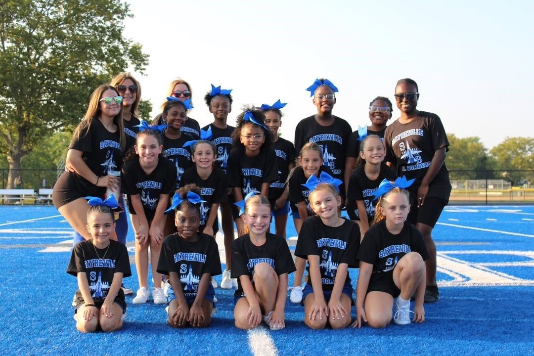 Cheerleading team in black and blue uniforms on a blue field; posing for a photo.