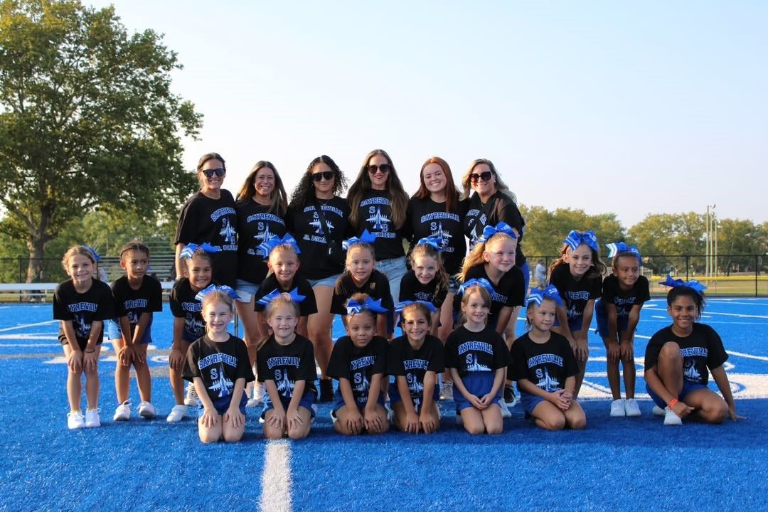 Cheerleaders in black and blue uniforms on a blue football field.