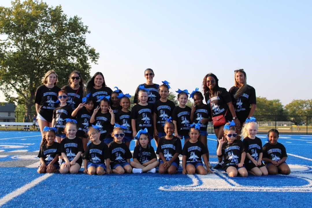 Cheerleading team posing on a blue track, wearing black shirts and blue bows.