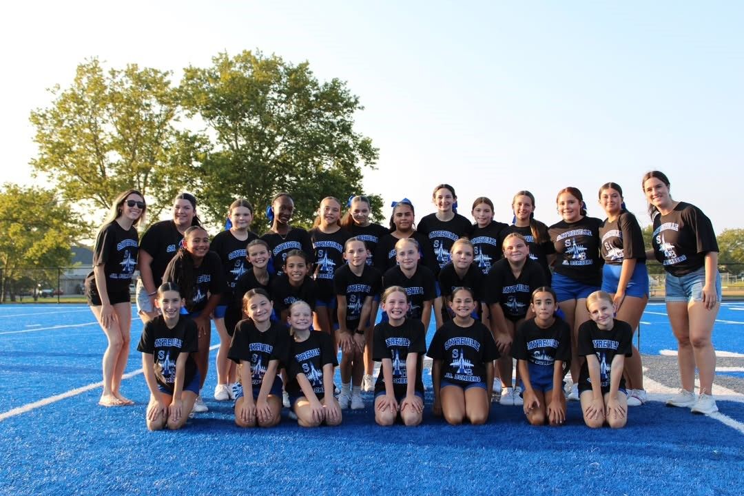 A group of cheerleaders wearing black shirts and shorts on a blue turf field.