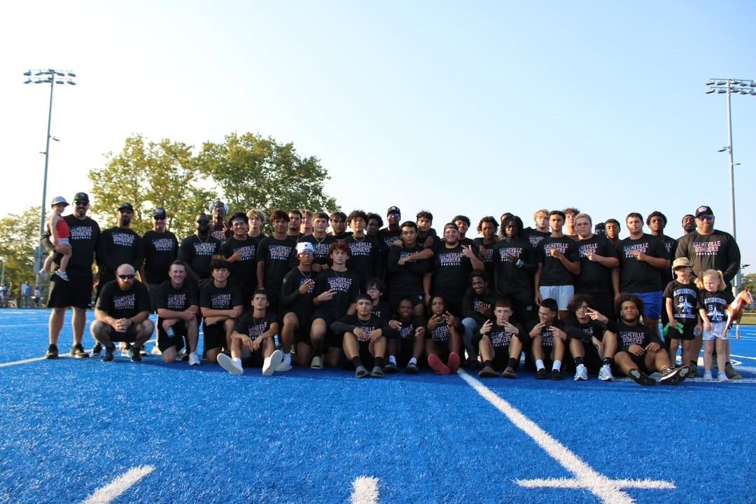 Group of people, mostly young adults, pose on a blue field in sportswear.