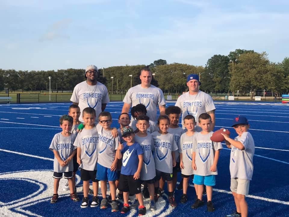 Youth football team posing on a blue track with coaches. They wear gray shirts and shorts.