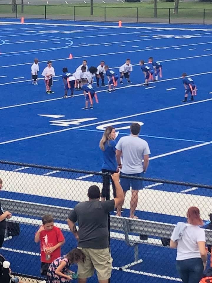 Youth flag football game on a blue field. Spectators watch from the sidelines.