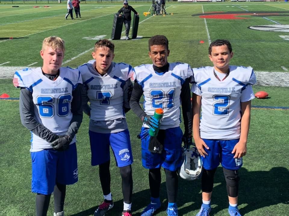 Four football players in blue and white uniforms standing on a green field.