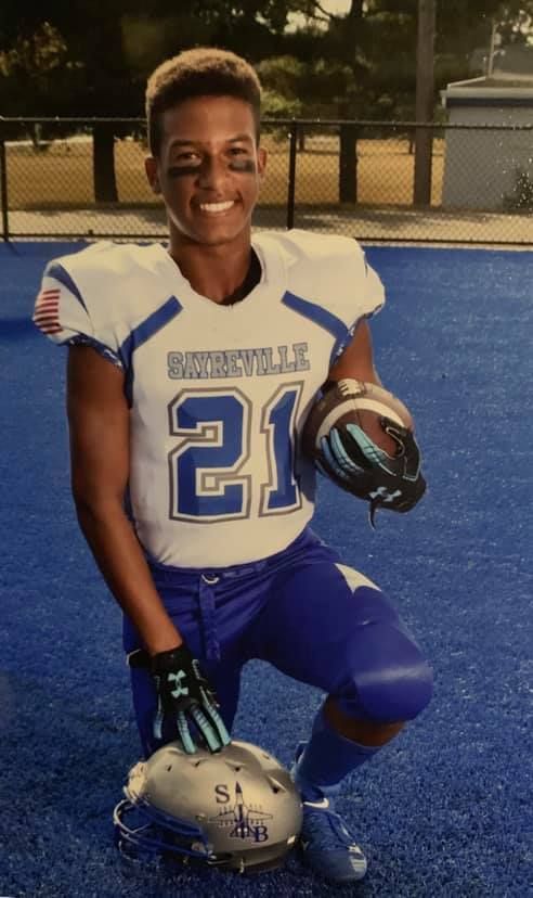 Football player kneeling, holding helmet and ball, wearing blue and white uniform with the number 21.