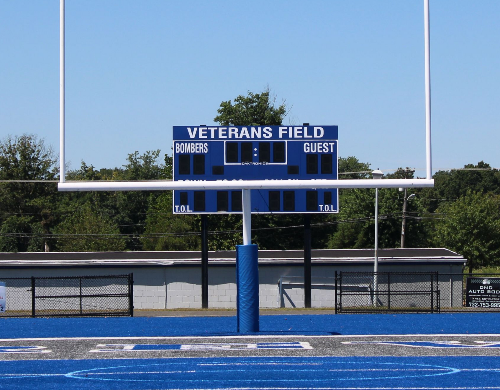 Football goal post and scoreboard at Veterans Field, blue track and clear sky.