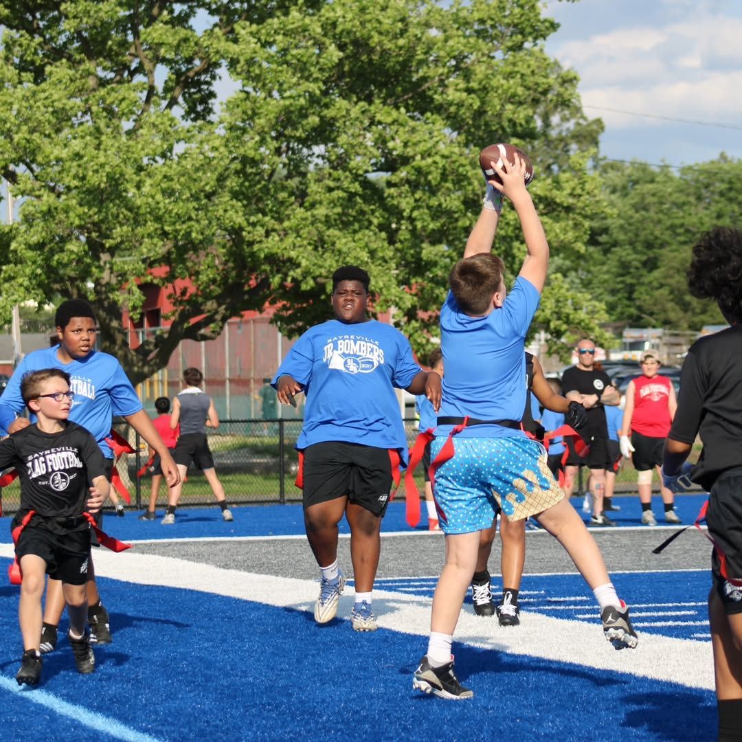 Football players huddle around a football, reaching hands together, blue sky backdrop.