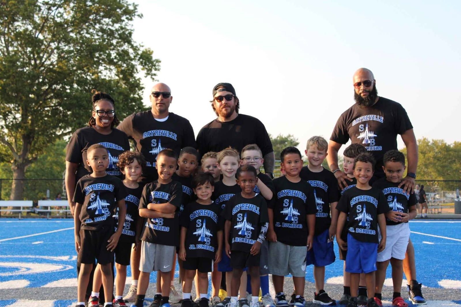 Youth football team and coaches wearing matching black shirts on a blue track.