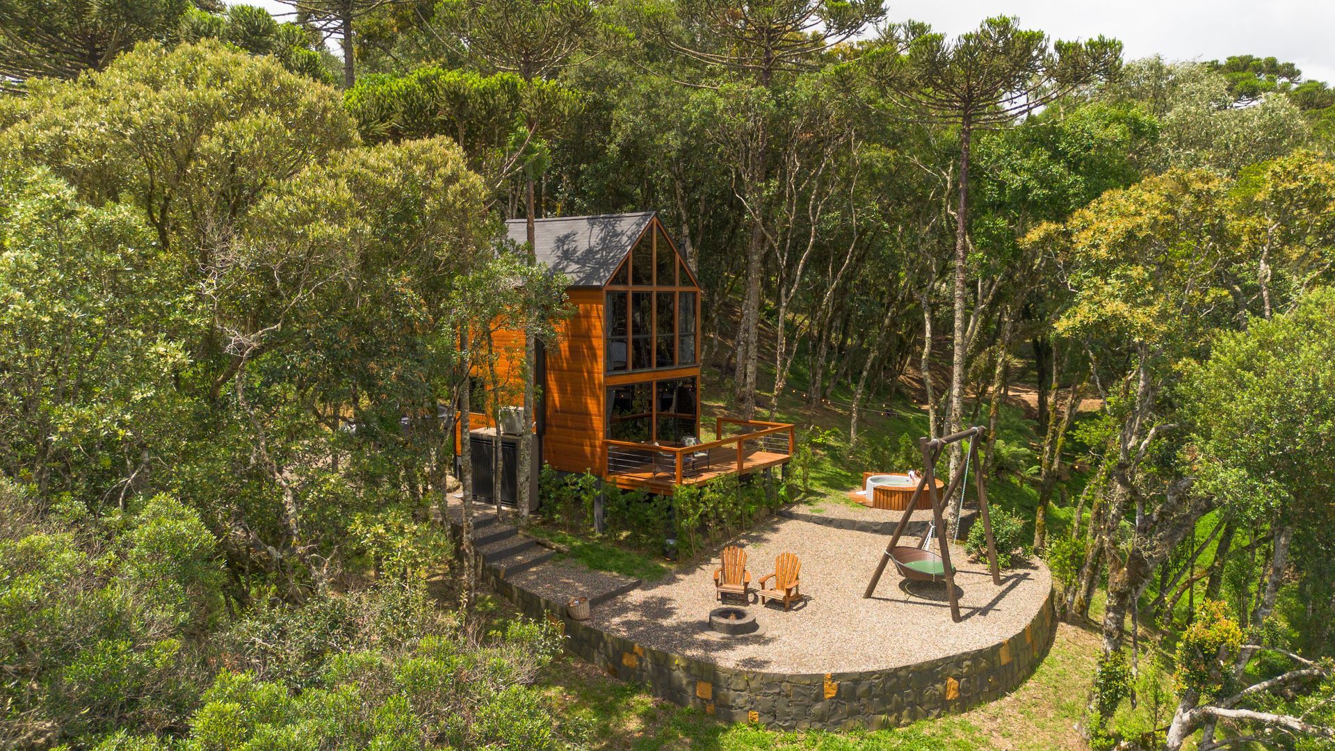 Cabana de madeira aninhada em meio a árvores verdejantes, com pátio de pedra e lareira externa.