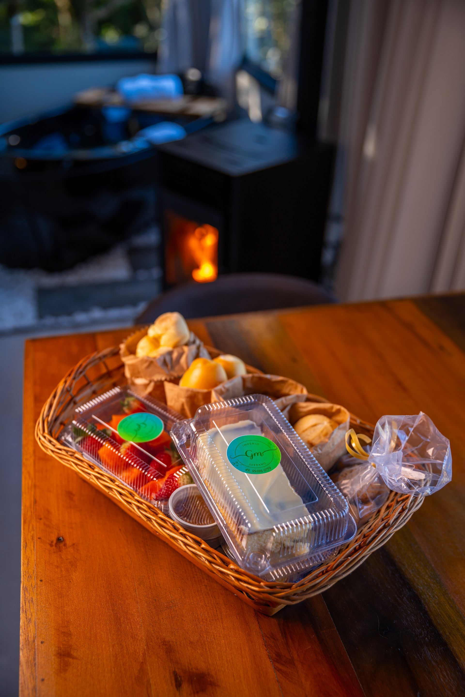 Cesta de alimentos sobre uma mesa de madeira, lareira ao fundo, luz aconchegante.