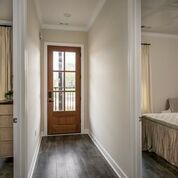Narrow hallway with dark wood floor, wooden door, and rooms on either side.