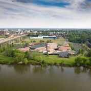 Aerial view of a campus and buildings along a river with a bridge, under a blue sky.