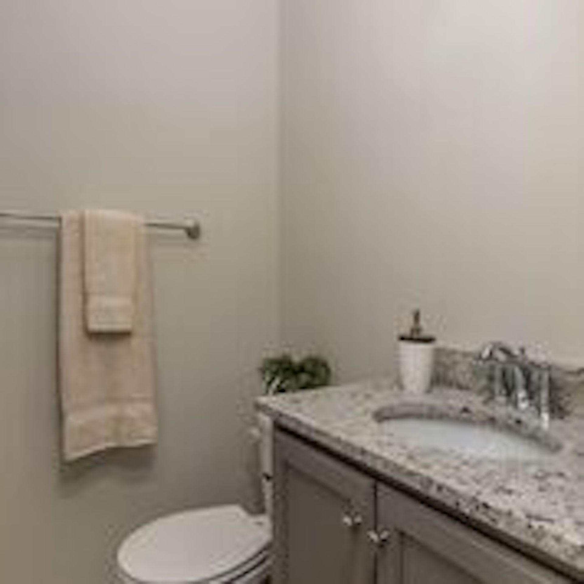 Bathroom with a vanity, toilet, and towel rack. Light gray walls, granite countertop, and gray cabinets.