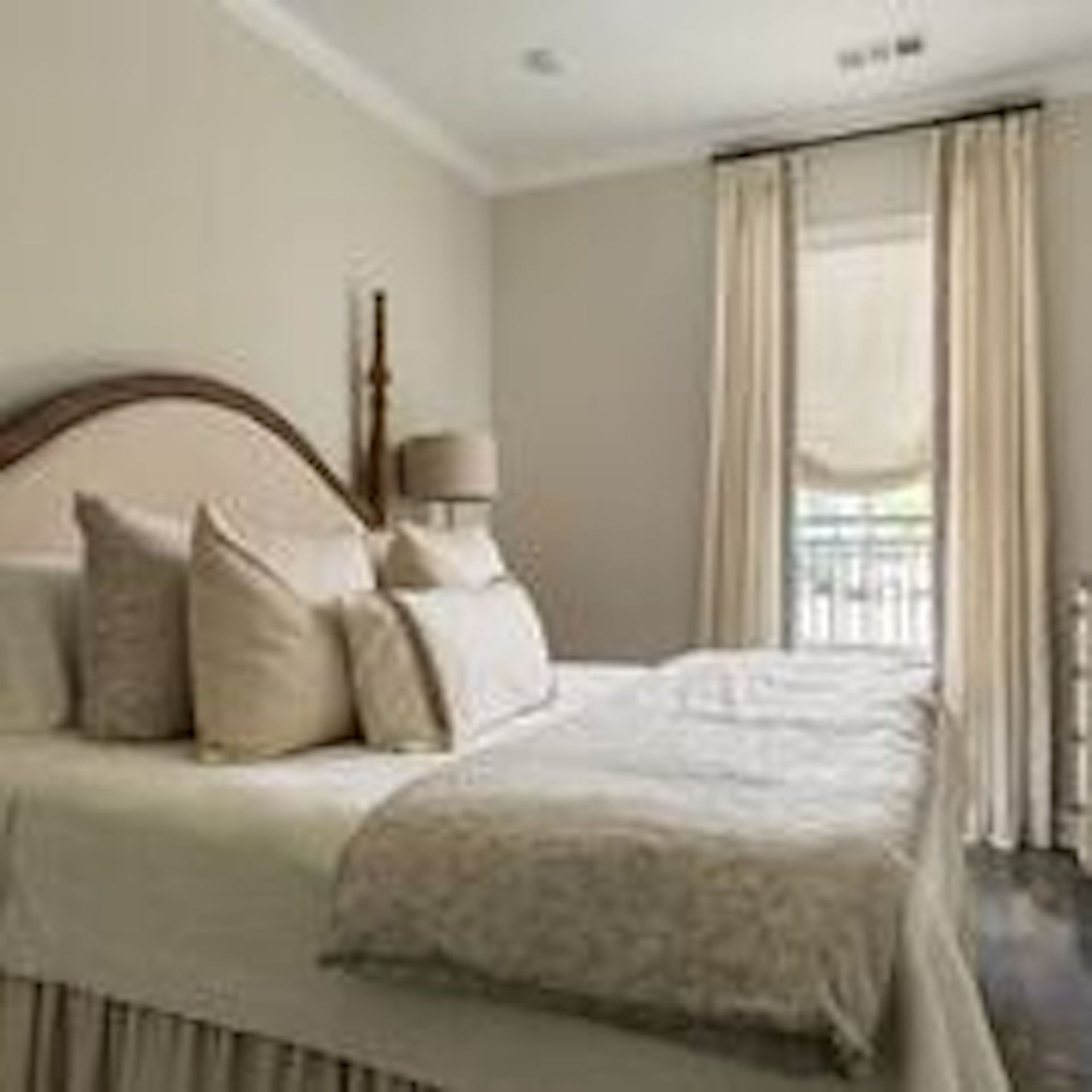 Bedroom with bed, pillows, cream-colored comforter, and curtains.