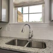 Stainless steel kitchen sink with faucet and window, light countertop, and white subway tile backsplash.