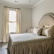 Bedroom with bed, curtains, and a window. Neutral tones with a decorative bedspread and pillows.