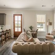 Living room with tufted sofa, kitchen counter with stools, and wooden door.