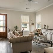 Living room with cream-colored furniture, dark wood floors, and a brown door; a rustic console table is against the wall.