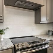 Kitchen with stove, gray cabinets, white tiled backsplash, and granite countertop.