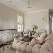 Living room with button-tufted sofa, two armchairs, distressed cabinet, coffee table, and window with a Roman shade.