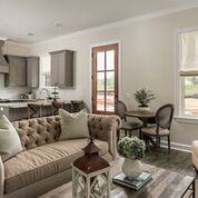 Living room with tufted sofa, kitchen cabinets, and a dining area, neutral colors.