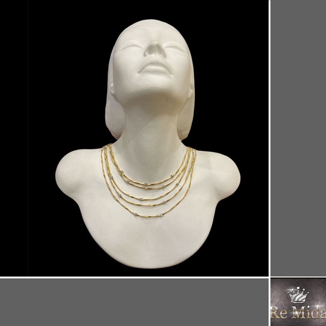 Busto in marmo bianco con occhi chiusi e collane dorate a strati, su sfondo nero.