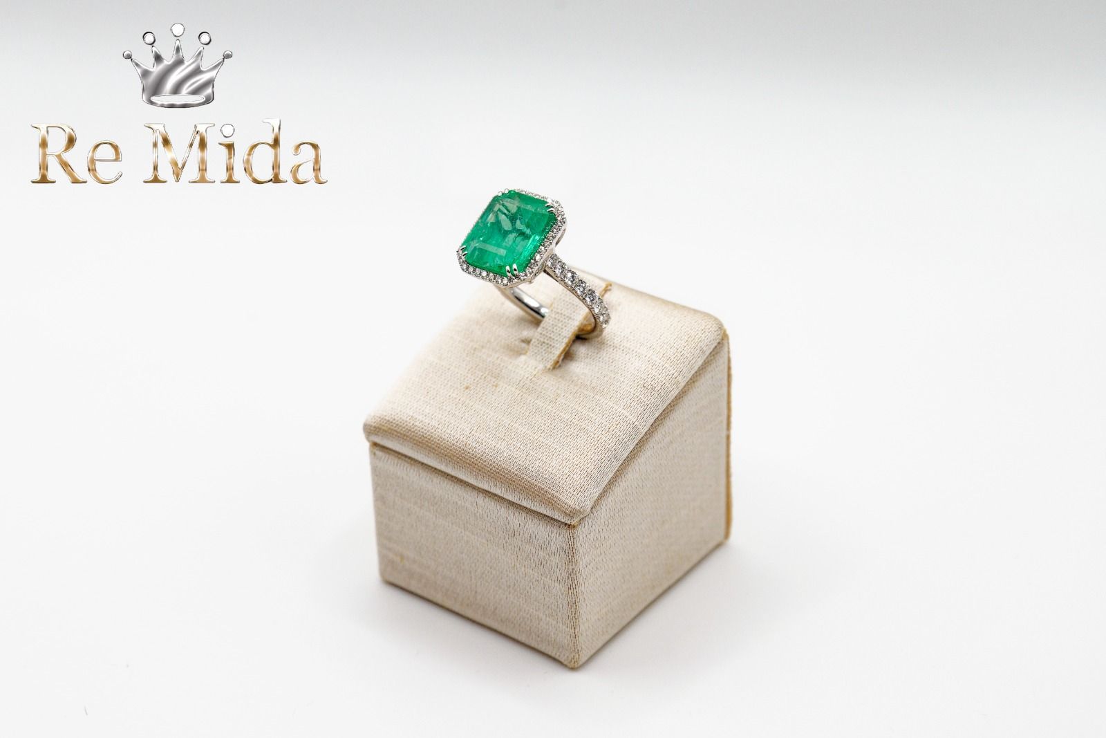 Anello con smeraldo su un espositore beige, con diamanti sulla fascia.