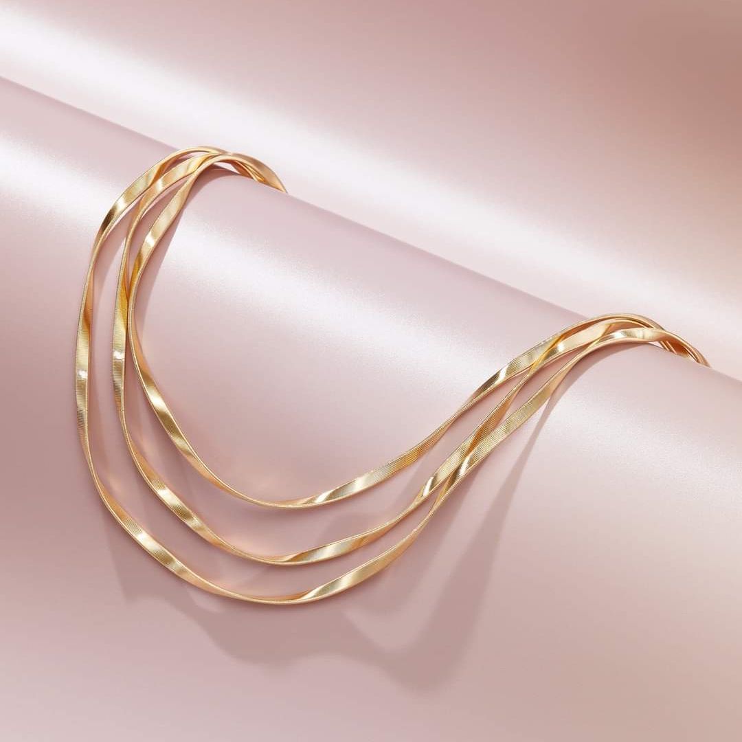 Collana a strati in oro su sfondo di seta rosa.