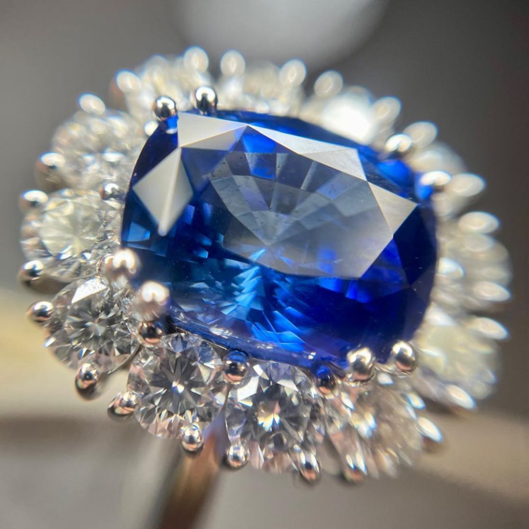 Anello con alone di diamanti e zaffiri blu, primo piano. Pietra centrale in zaffiro blu brillante, circondata da diamanti bianchi.