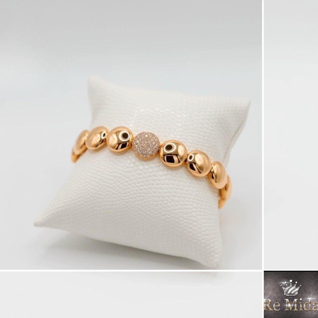 Bracciale in oro con perle rotonde e cave e una gemma centrale scintillante, esposto su un cuscino bianco.