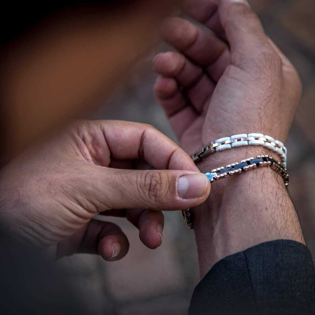 Persona che si sistema un braccialetto argentato e nero al polso, con un braccialetto bianco sopra.