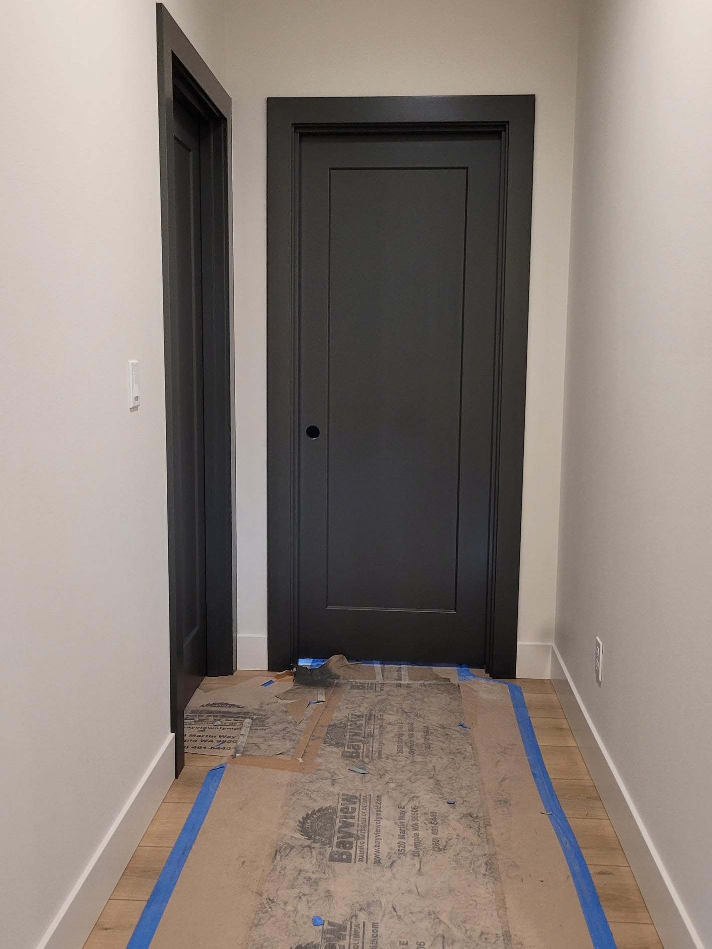 A hallway with two black doors and a blue tape on the floor.
