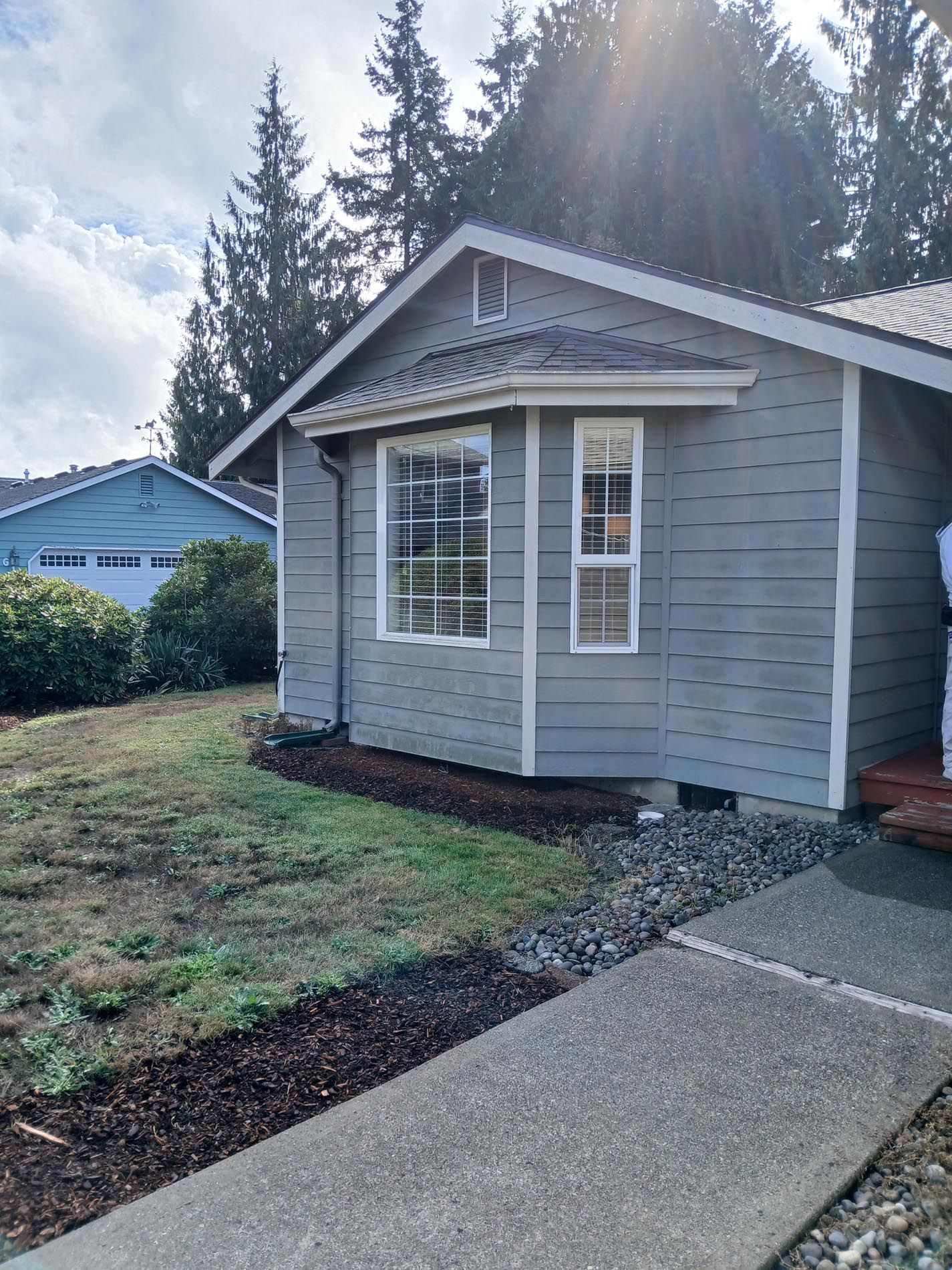 A small gray house with a concrete sidewalk in front of it.