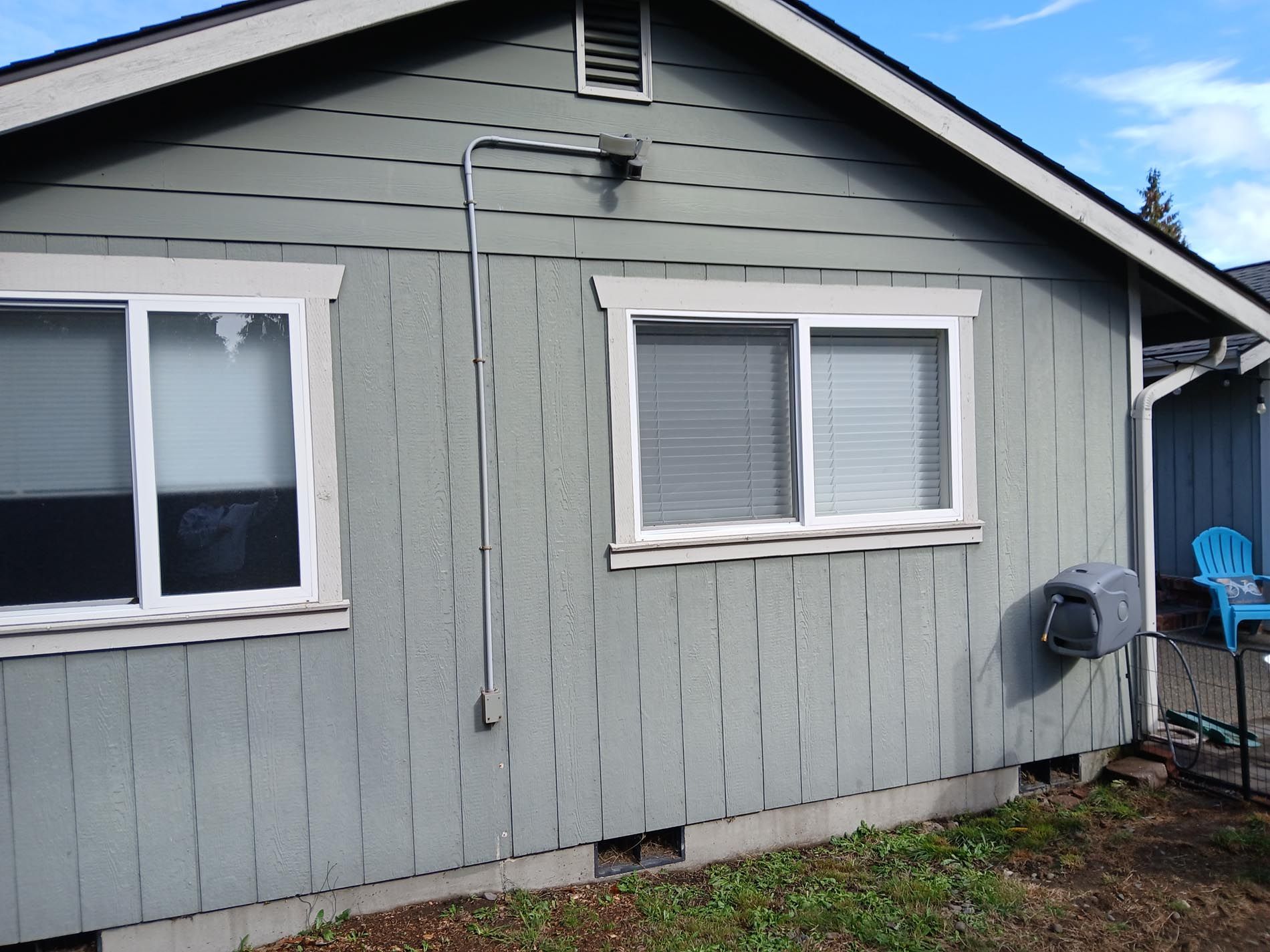 A gray house with two windows and a blue chair