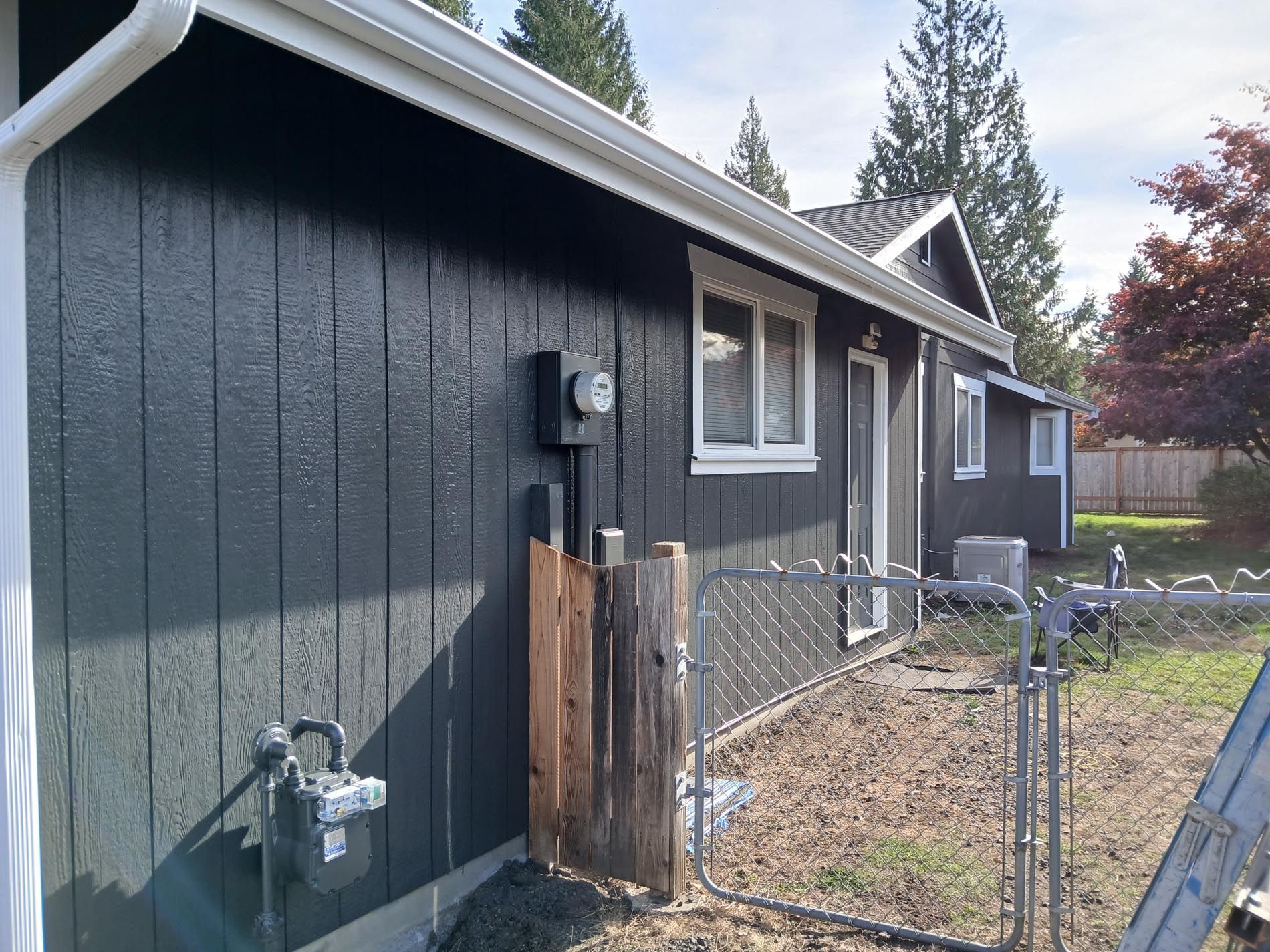A black house with white trim and a ladder in front of it
