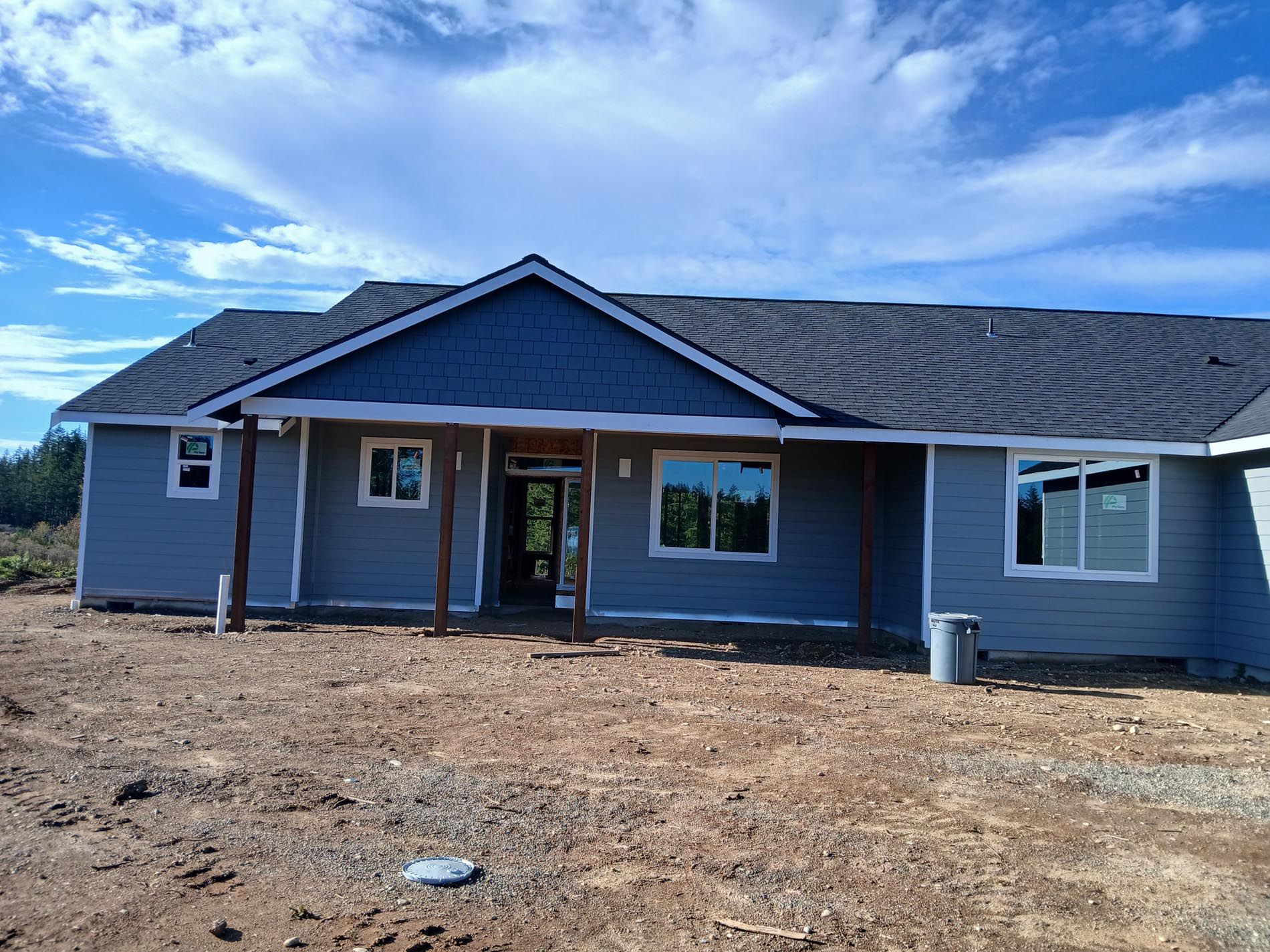 A blue house with a gray roof is sitting in the middle of a dirt field.