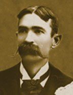 A man with a mustache is wearing a suit and tie.