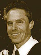A man in a suit and tie is smiling in a black and white photo.