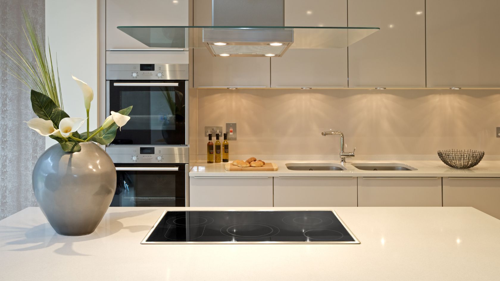 Modern kitchen with white cabinets, island, stovetop, and silver vase with flowers.