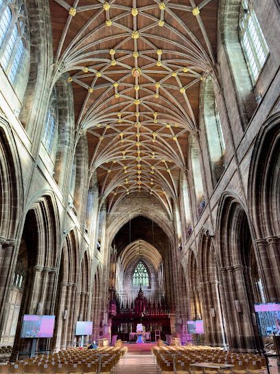 Inside a cathedral, high vaulted ceiling with ornate pattern. Rows of pews face the altar.