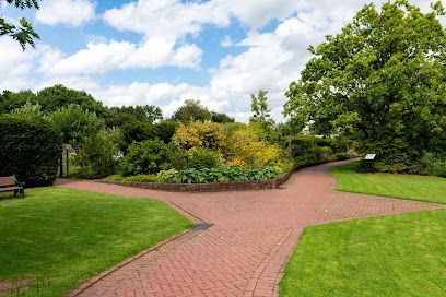 Brick pathways split in a green park with lush trees and a cloudy sky.