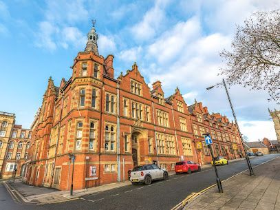 Red brick building with ornate details and a clock tower, cars parked on street.