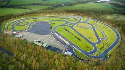 Aerial view of a go-kart racing track with a complex layout. Green grass surrounds the black asphalt track.